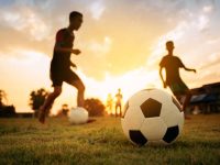 action sport outdoors of a group of kids having fun playing soccer football on the dirt field.